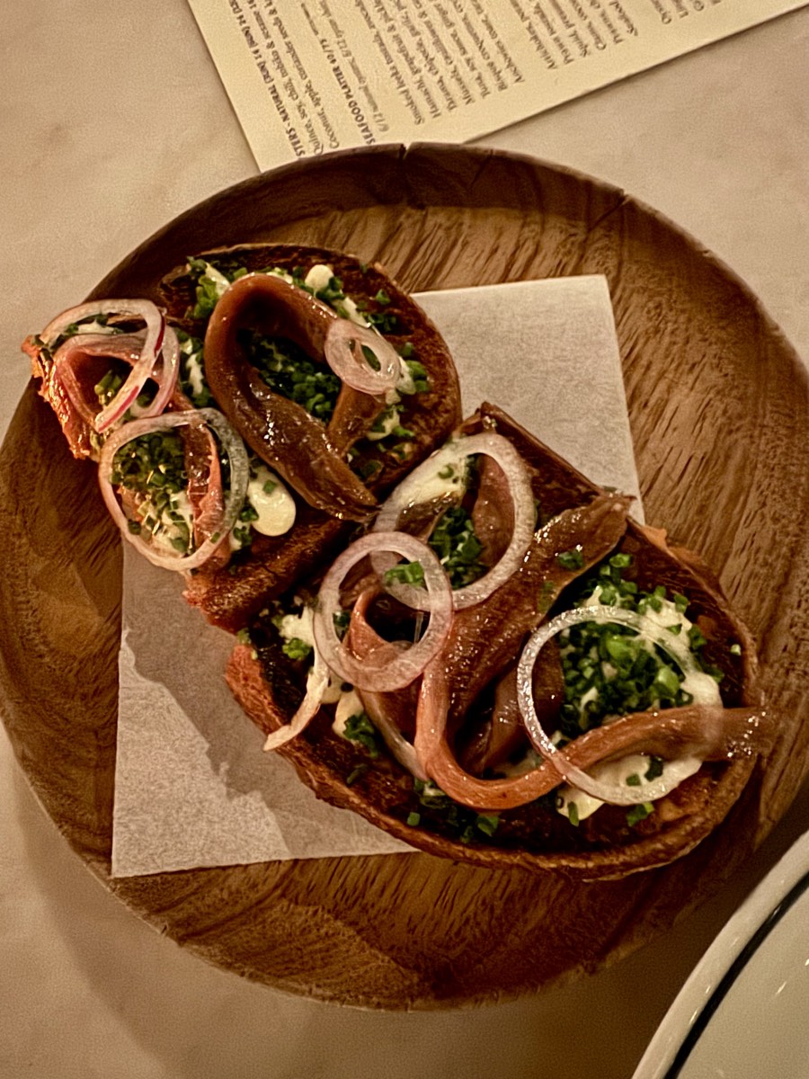 Twee tostadas met ansjovis, rode ui, bieslook en room op een houten bord